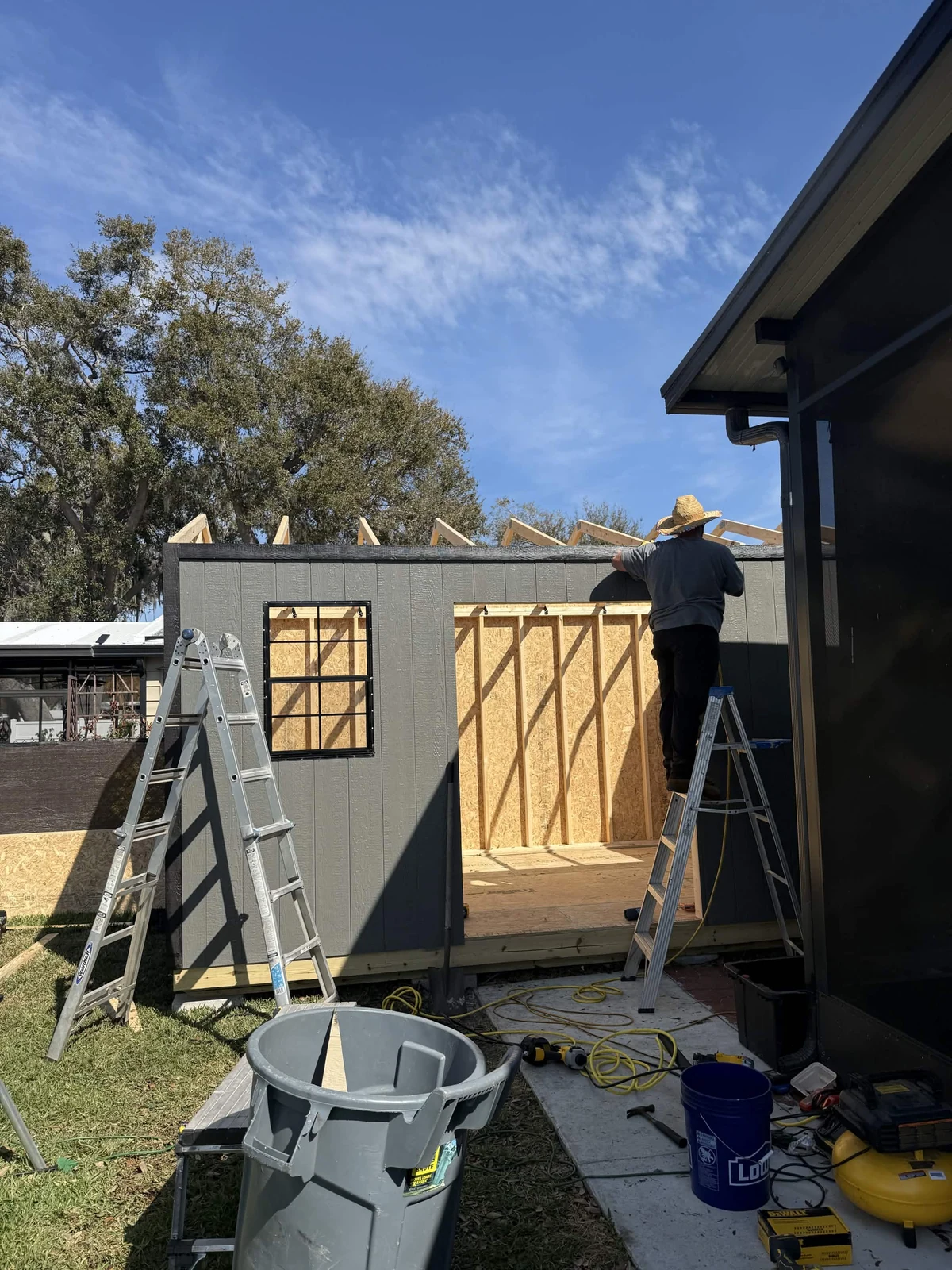 Another exterior view of the 10 by 16-foot shed showing a window, doorway, dark wall finish, and roof framing above the wall