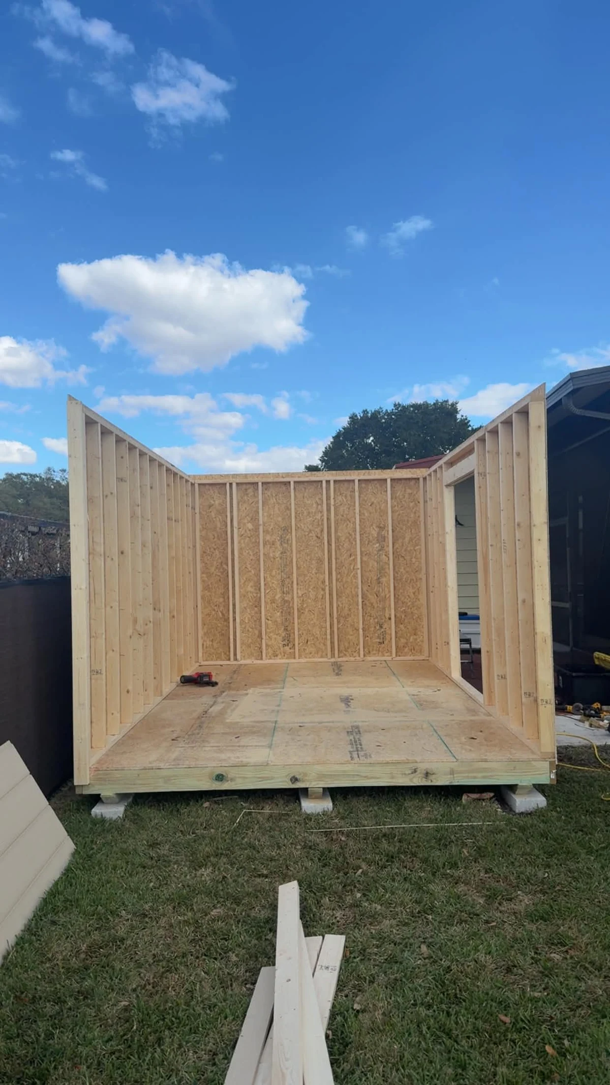 Interior view of the 10 by 16-foot shed with three framed walls standing, the floor visible, and an opening in the right wall