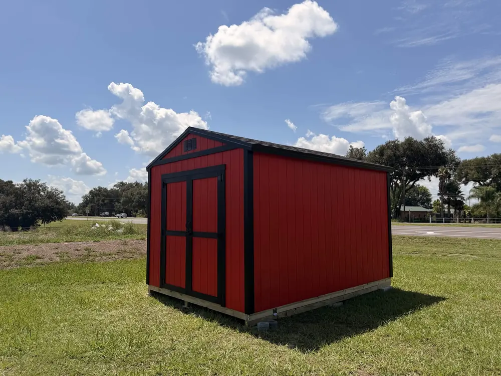 Red barn-style custom shed with black trim in an open yard
